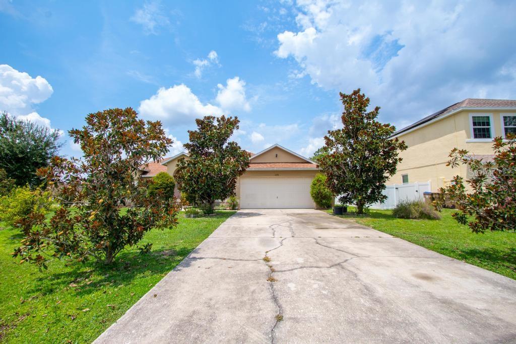A single-story house with a two-car garage and a cracked concrete driveway — 1126 LAVAUR COURT, KISSIMMEE, FL