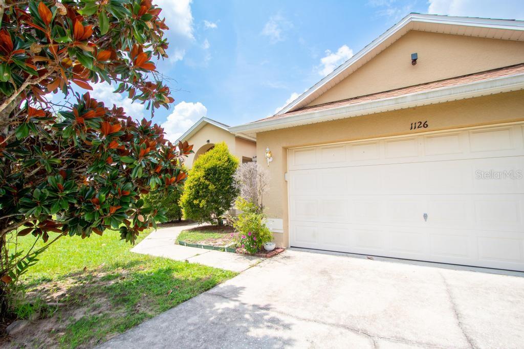 A beige house exterior features a white two-car garage and a landscaped front yard — 1126 LAVAUR COURT, KISSIMMEE, FL