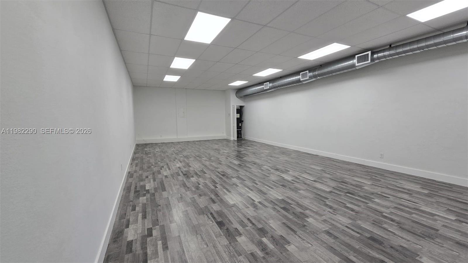 An empty commercial room features white walls, a drop ceiling, and grey wood-look flooring — 957 SW 122nd Ave # 957, Miami FL 33184, MIAMI, FL