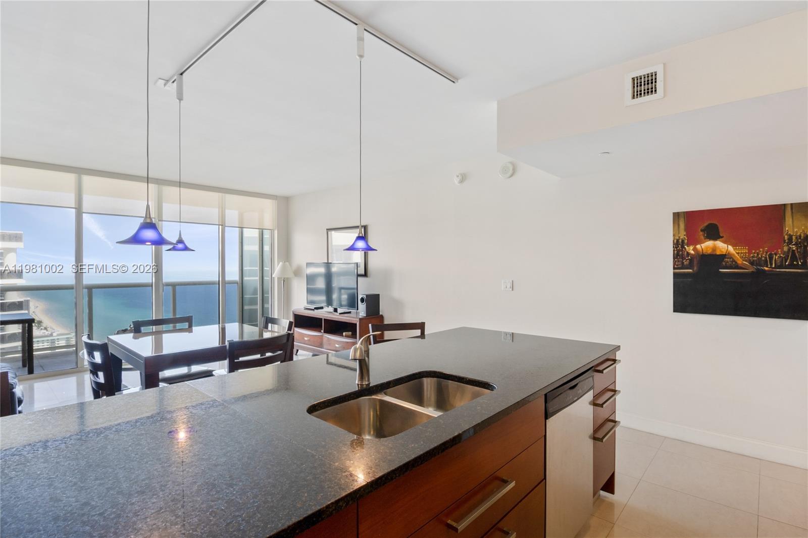 A kitchen island with a dark countertop and sink overlooks a dining area and ocean — 1830 S OCEAN DR # 4409, Hallandale Beach FL 33009, HALLANDALE BEACH, FL