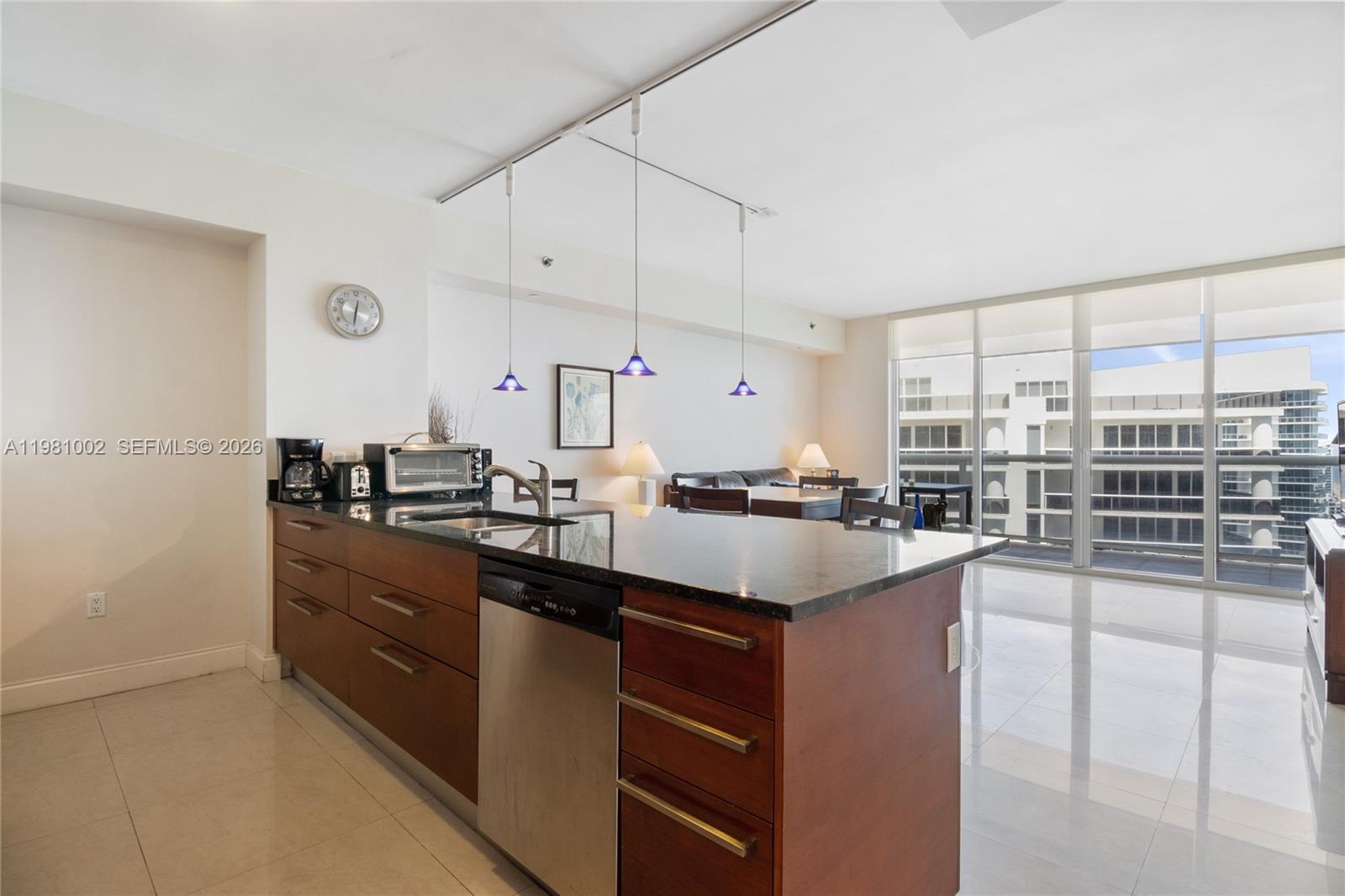 A modern kitchen island with dark countertops and wood cabinetry sits in an open-plan apartment — 1830 S OCEAN DR # 4409, Hallandale Beach FL 33009, HALLANDALE BEACH, FL