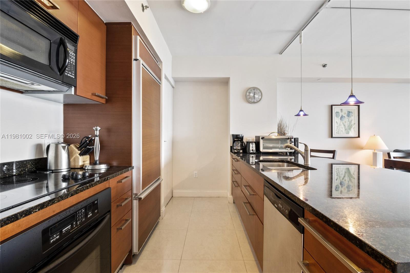 A galley-style kitchen features wood cabinetry, dark granite countertops, and stainless steel appliances — 1830 S OCEAN DR # 4409, Hallandale Beach FL 33009, HALLANDALE BEACH, FL