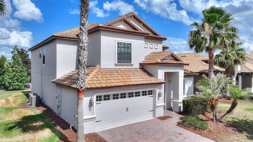A two-story house with a tiled roof, a white garage, and palm trees in the yard — 1315 MOSS CREEK LN, DAVENPORT, FL