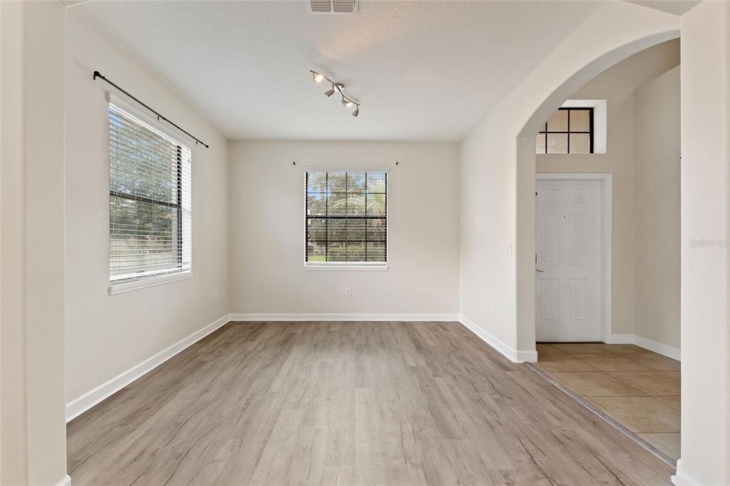 An empty room with light-colored walls, wood-look flooring, and a view of the entryway — 1315 MOSS CREEK LN, DAVENPORT, FL