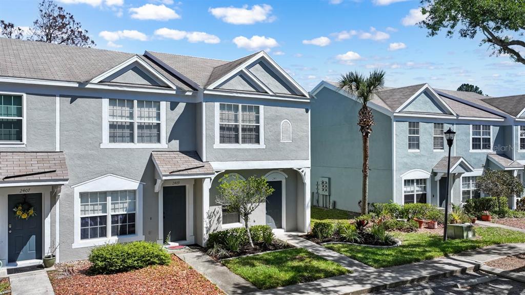 Exterior view of two-story townhomes with gray stucco siding and gabled rooflines under a blue sky — 2411 LAKE WOODBERRY CIRCLE, BRANDON, FL