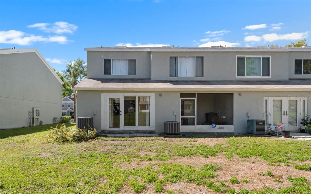 The exterior rear view of a two-story townhouse features a screened patio and HVAC units — 2411 LAKE WOODBERRY CIRCLE, BRANDON, FL
