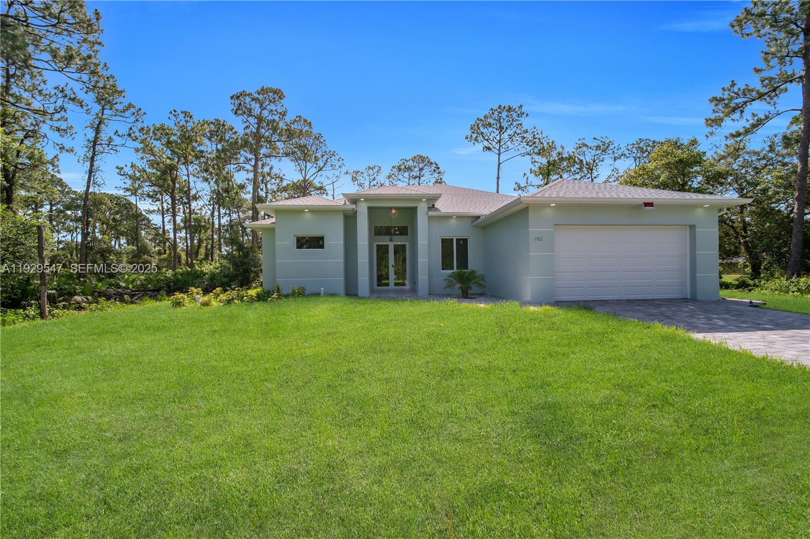 A light green single-story house with a two-car garage sits on a grassy lot — 1912 Roosevelt, Lehigh Acres FL 33972, LEHIGH ACRES, FL