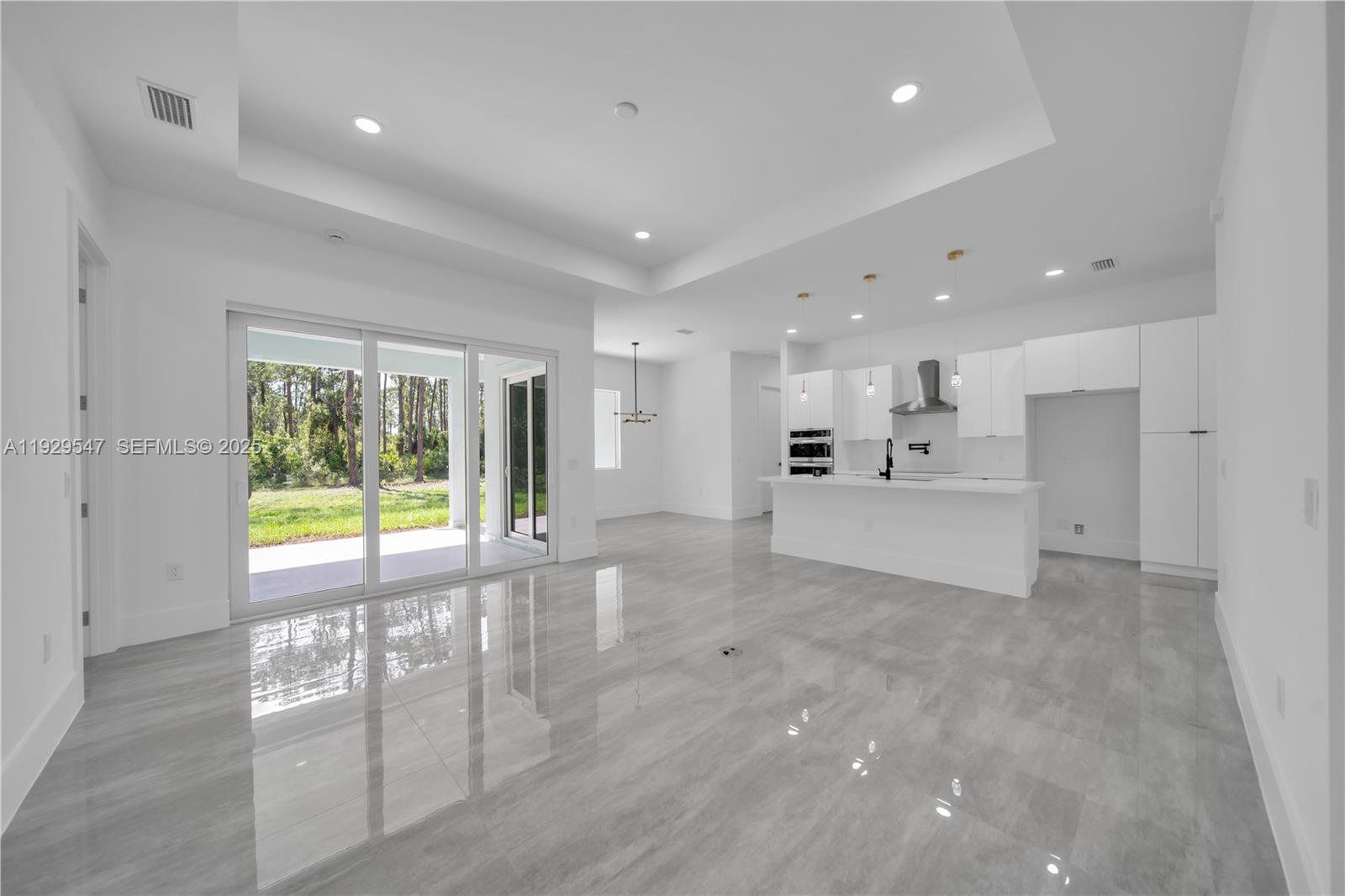 This open-concept kitchen and living area features white cabinetry, a kitchen island, and tile flooring — 1912 Roosevelt, Lehigh Acres FL 33972, LEHIGH ACRES, FL