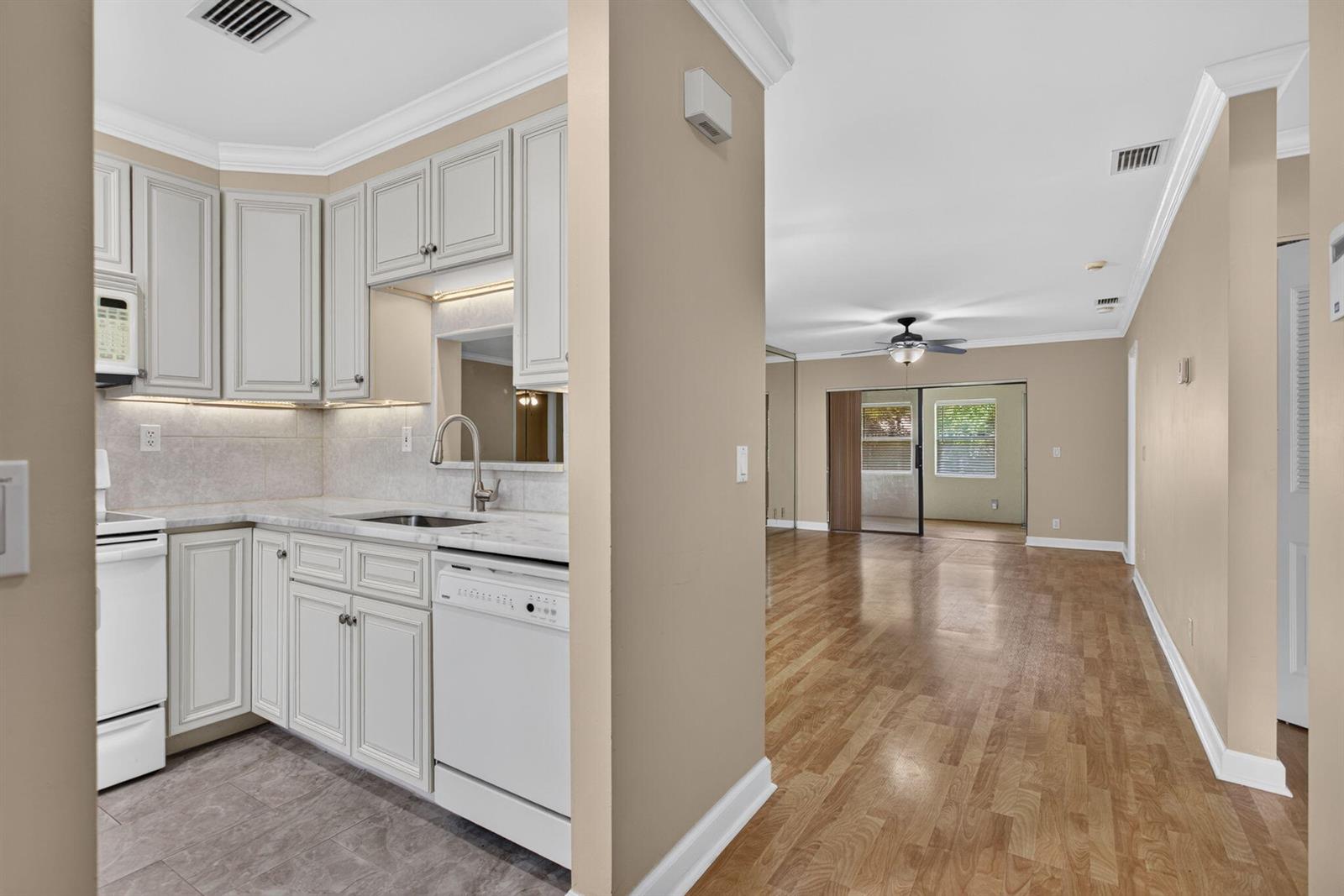 A kitchen with light-colored cabinets and stone countertops opens into a living area with wood floors — 353 NW 36th Avenue, Deerfield Beach FL 33442, DEERFIELD BEACH, FL
