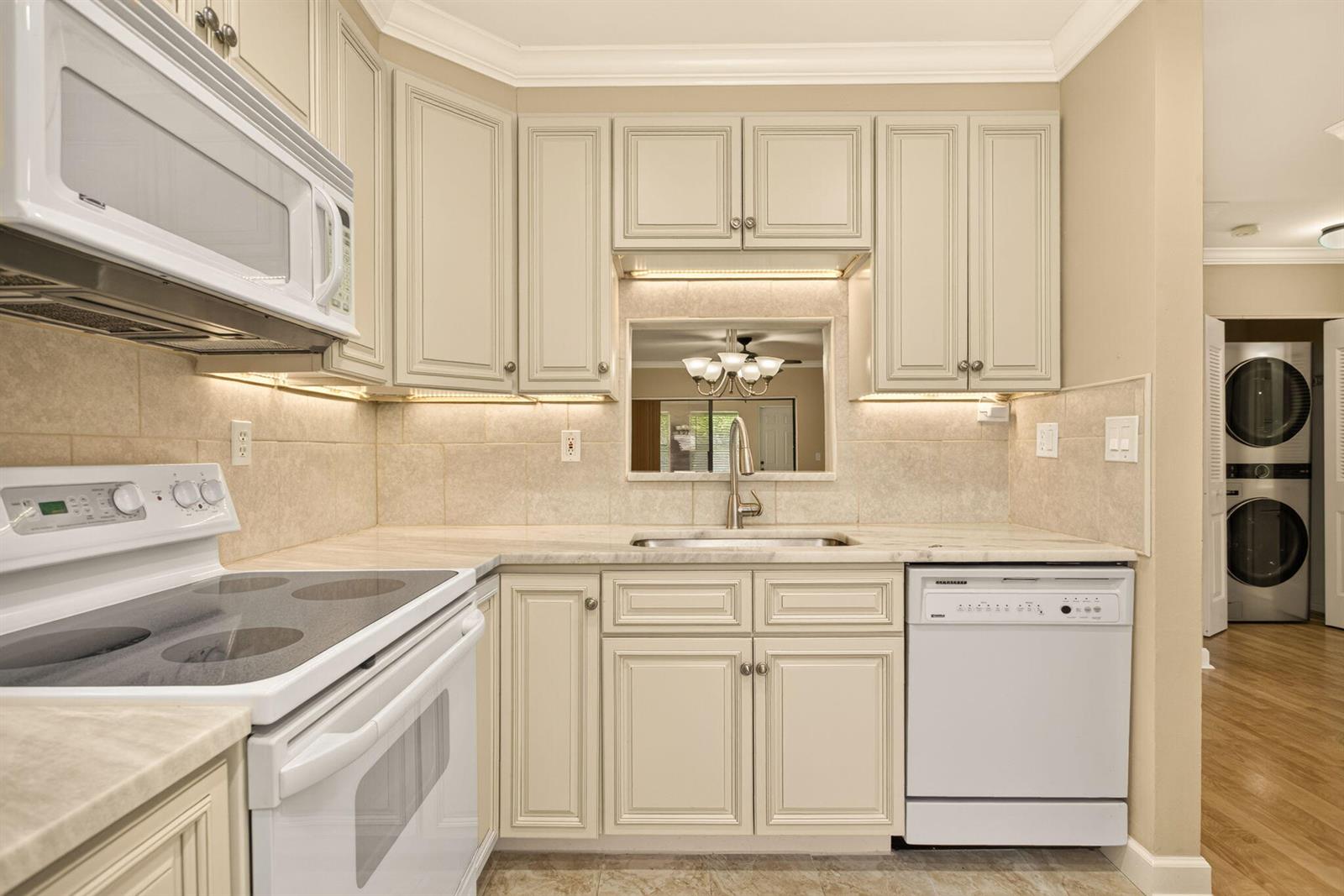 A kitchen features cream-colored cabinets, a white stove, a dishwasher, and a pass-through window — 353 NW 36th Avenue, Deerfield Beach FL 33442, DEERFIELD BEACH, FL