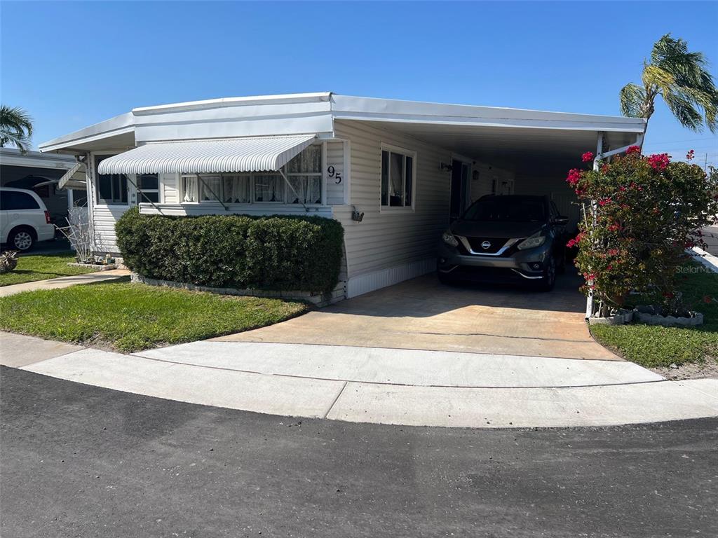 A single-story manufactured home with a carport, driveway, and a small front lawn — 11300 124TH AVENUE UNIT 95, LARGO, FL