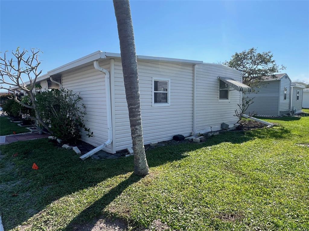 The exterior side view of a light-colored mobile home features vinyl siding and a palm tree — 11300 124TH AVENUE UNIT 95, LARGO, FL
