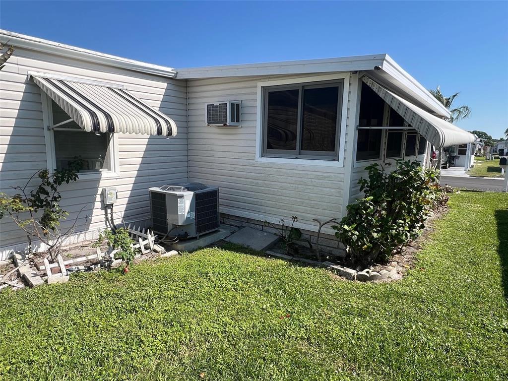The exterior of a light-colored mobile home features window awnings and an air conditioning unit — 11300 124TH AVENUE UNIT 95, LARGO, FL