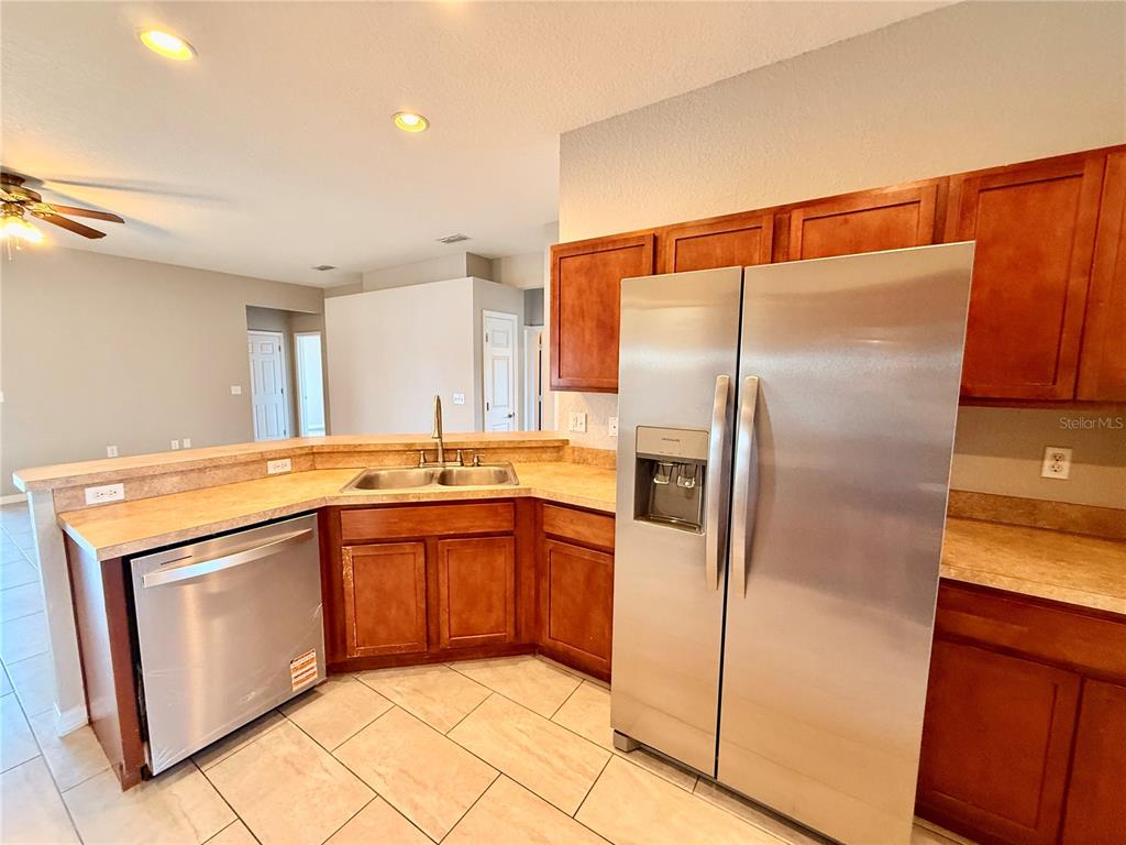 A kitchen features wood cabinets, stainless steel appliances, and a corner sink with tile flooring — 1192 NORMANDY HEIGHTS CIRCLE, WINTER HAVEN, FL