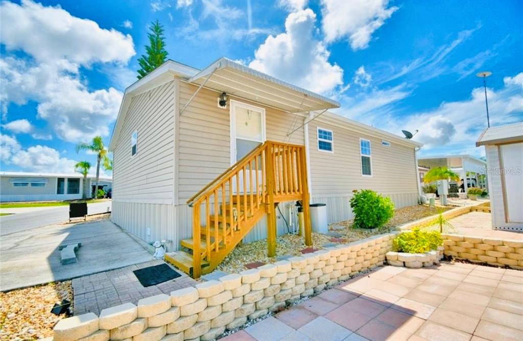 A tan mobile home features a wooden staircase leading to the front door — 251 PATTERSON ROAD UNIT H29, HAINES CITY, FL
