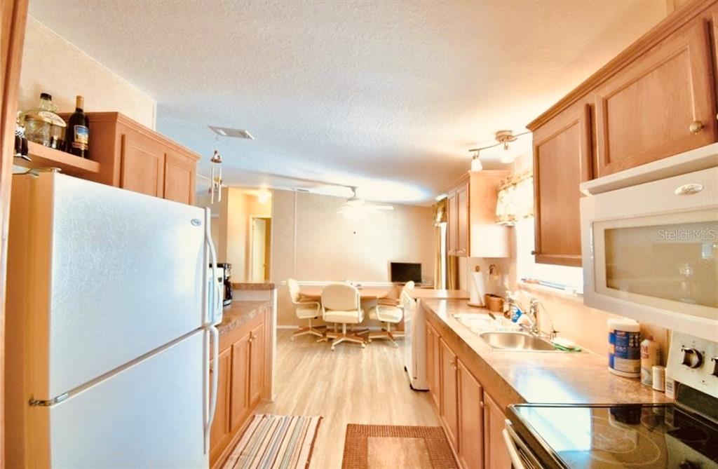 A kitchen with wood cabinets, white appliances, and a dining area in the background — 251 PATTERSON ROAD UNIT H29, HAINES CITY, FL