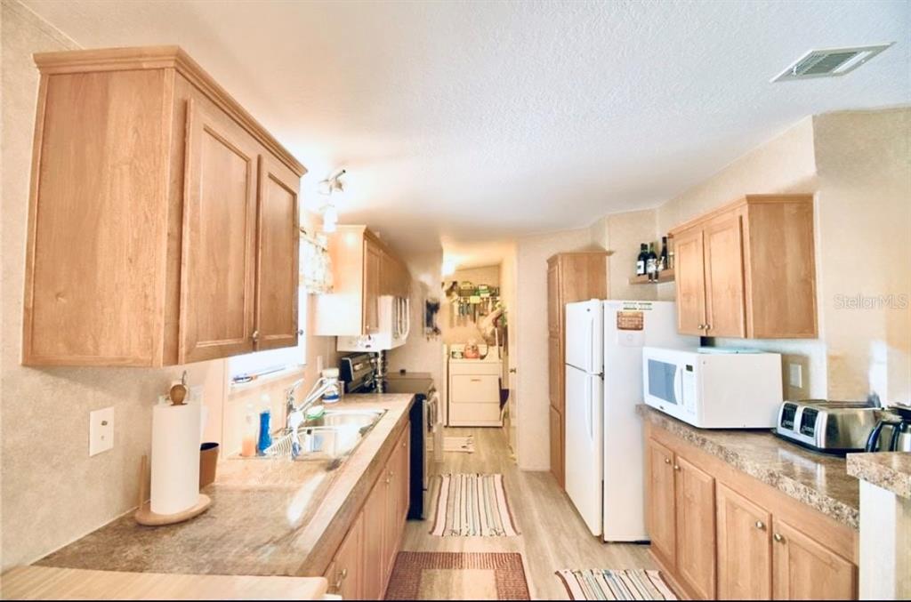 A galley kitchen features light wood cabinets, laminate countertops, and white appliances — 251 PATTERSON ROAD UNIT H29, HAINES CITY, FL