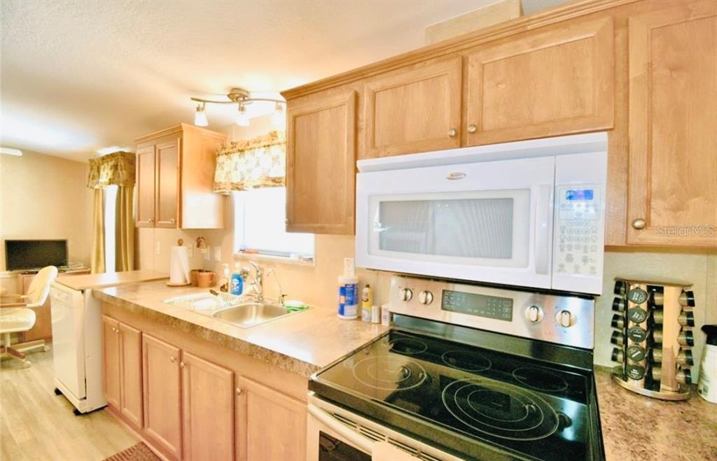 A kitchen features light wood cabinets, a white over-the-range microwave, and a black electric stove — 251 PATTERSON ROAD UNIT H29, HAINES CITY, FL