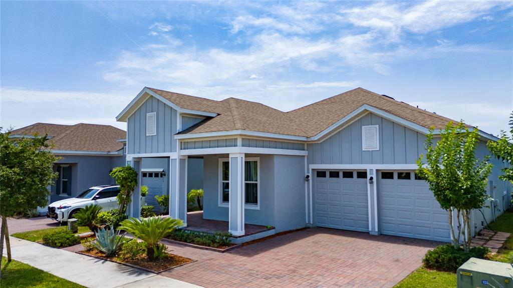 A light blue single-story house with a brick driveway, two-car garage, and covered entryway — 7687 BOWERY DRIVE, WINTER GARDEN, FL