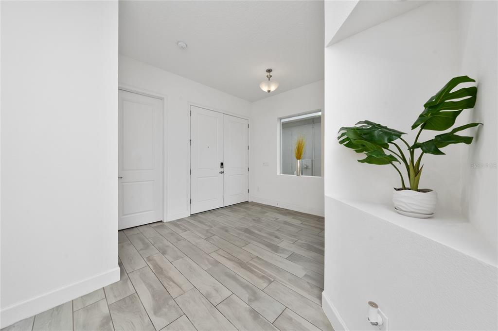 An entryway features white walls, light wood-look tile flooring, a double door, and a plant — 7687 BOWERY DRIVE, WINTER GARDEN, FL