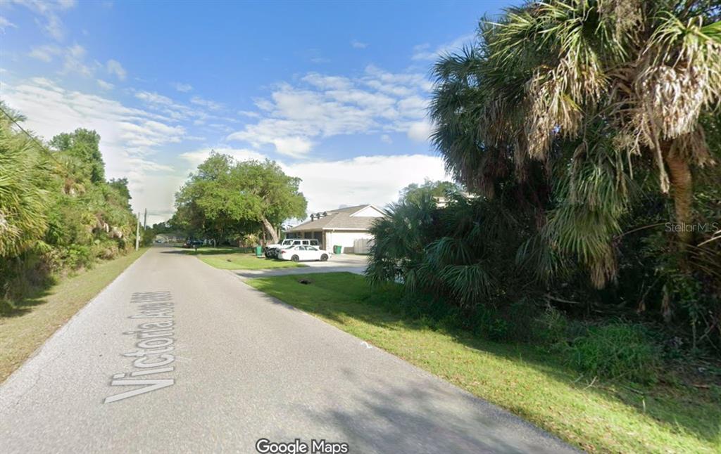A paved road leads past a residential house surrounded by trees and dense vegetation — 1031 VICTORIA AVENUE, PORT CHARLOTTE, FL