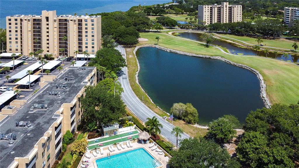 An aerial view shows apartment buildings, a swimming pool, a pond, and a golf course — 2616 COVE CAY DRIVE UNIT 506, CLEARWATER, FL