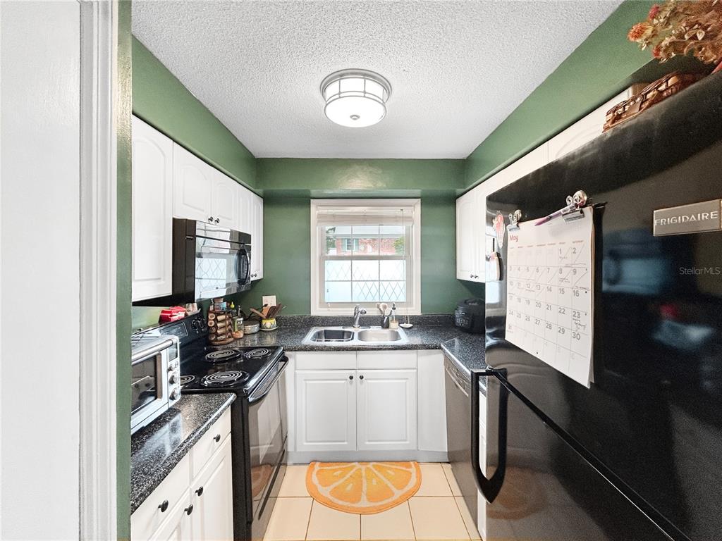 A galley kitchen features white cabinets, black appliances, dark countertops, and green walls — 116 GEORGETOWN DRIVE, CASSELBERRY, FL