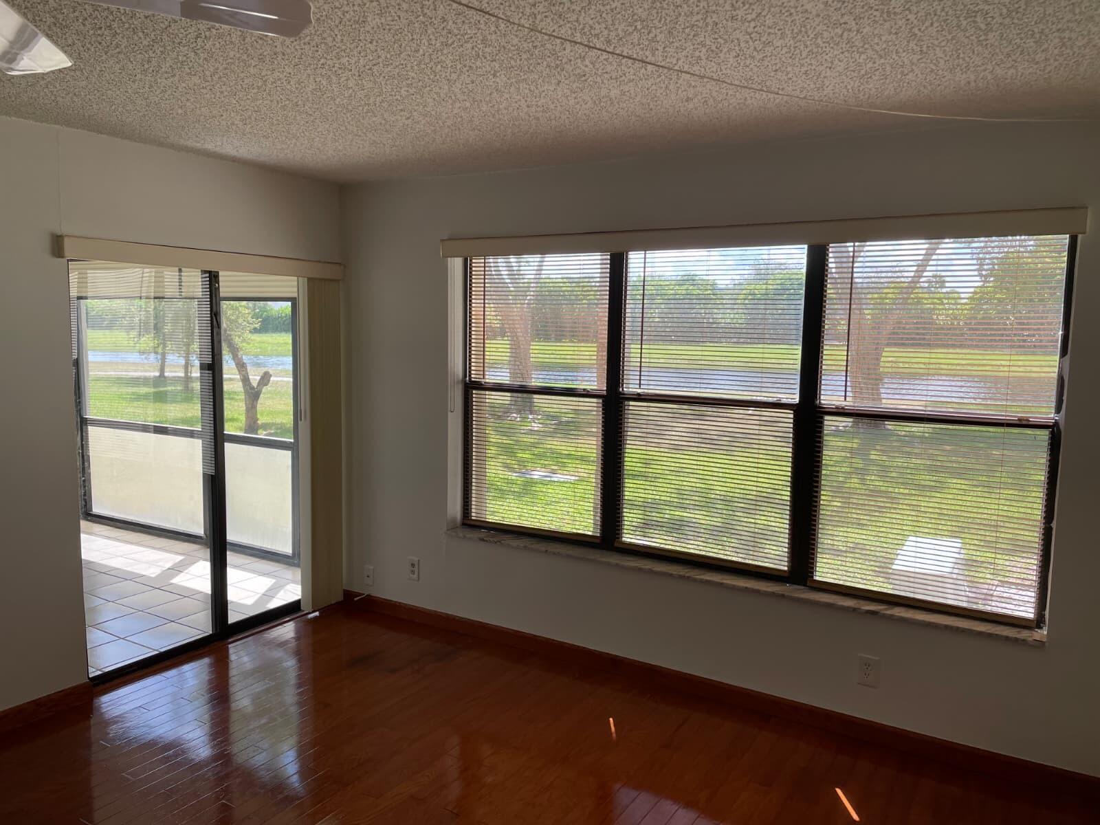 A room with hardwood floors, large windows with blinds, and a sliding glass door — 2322 S Cypress Bend Drive # 110, Pompano Beach FL 33069, POMPANO BEACH, FL