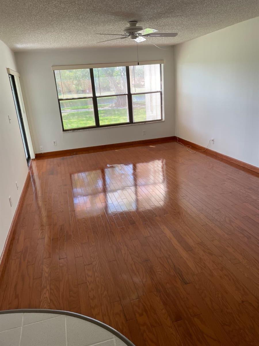 An empty room features glossy hardwood flooring, white walls, a ceiling fan, and large windows — 2322 S Cypress Bend Drive # 110, Pompano Beach FL 33069, POMPANO BEACH, FL