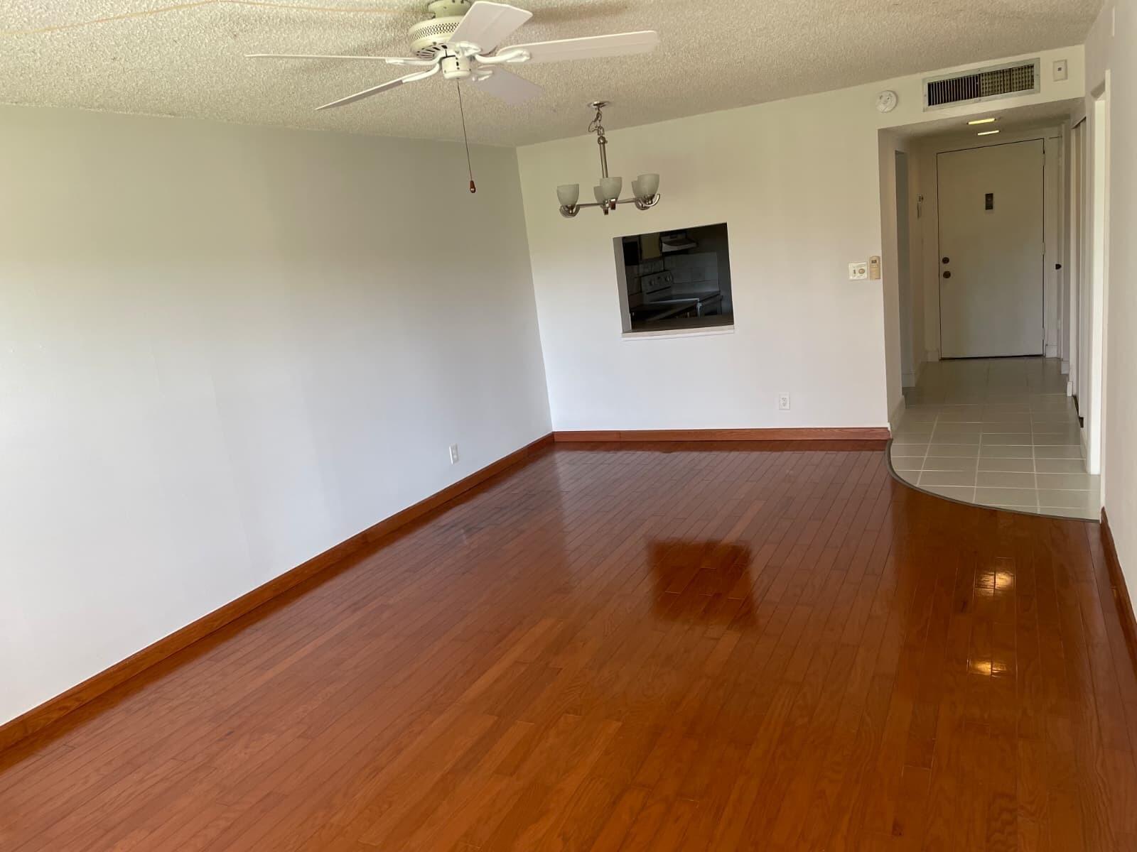 An empty living room with hardwood floors, a ceiling fan, and a kitchen pass-through window — 2322 S Cypress Bend Drive # 110, Pompano Beach FL 33069, POMPANO BEACH, FL