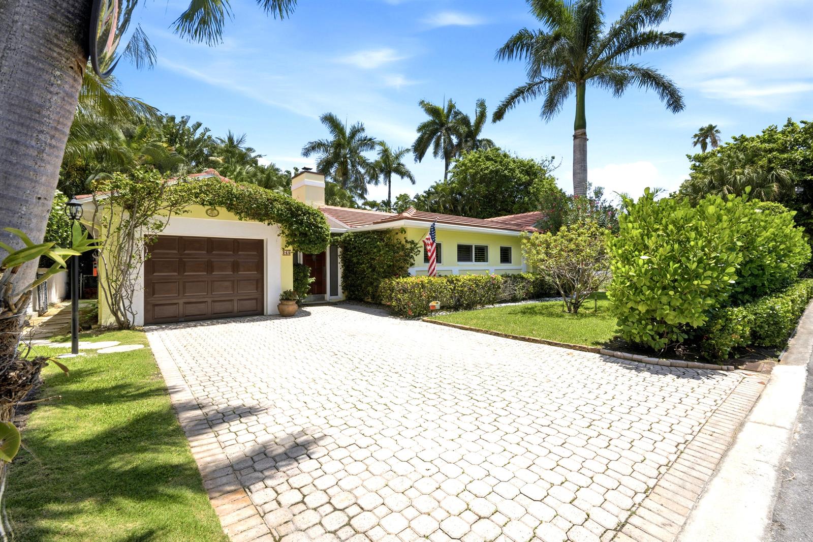 A yellow house with a brown garage door and a paved driveway sits among palm trees — 265 Fairview Road, Palm Beach FL 33480, PALM BEACH, FL