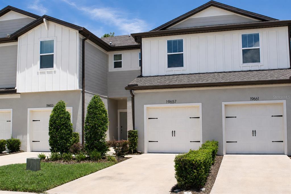 The exterior of a multi-unit townhouse complex features white garage doors and gray siding — 19657 SHADY OAK DRIVE, LAND O LAKES, FL