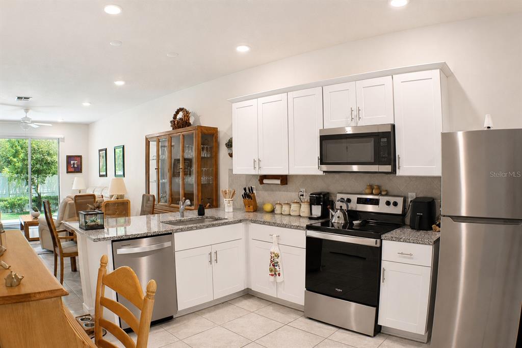 A kitchen with white cabinets, stainless steel appliances, and granite countertops opens to a living area — 19657 SHADY OAK DRIVE, LAND O LAKES, FL