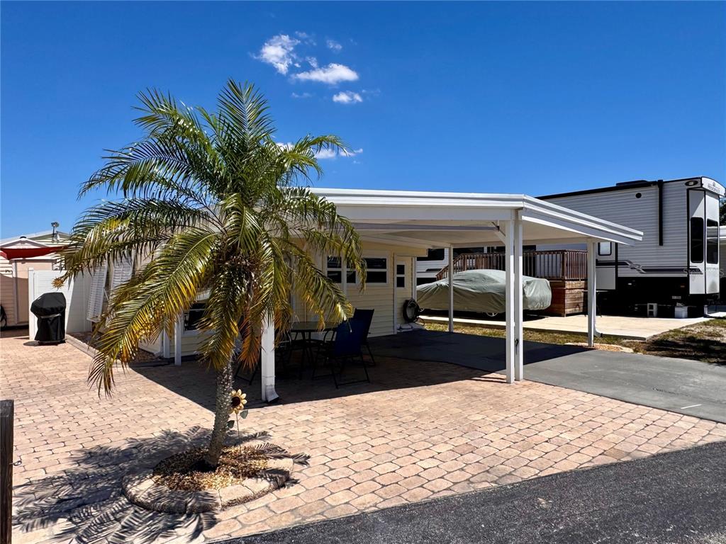 A light-colored mobile home features a paved patio, a palm tree, and a covered carport — 1475 FLAMINGO DRIVE UNIT 128, ENGLEWOOD, FL