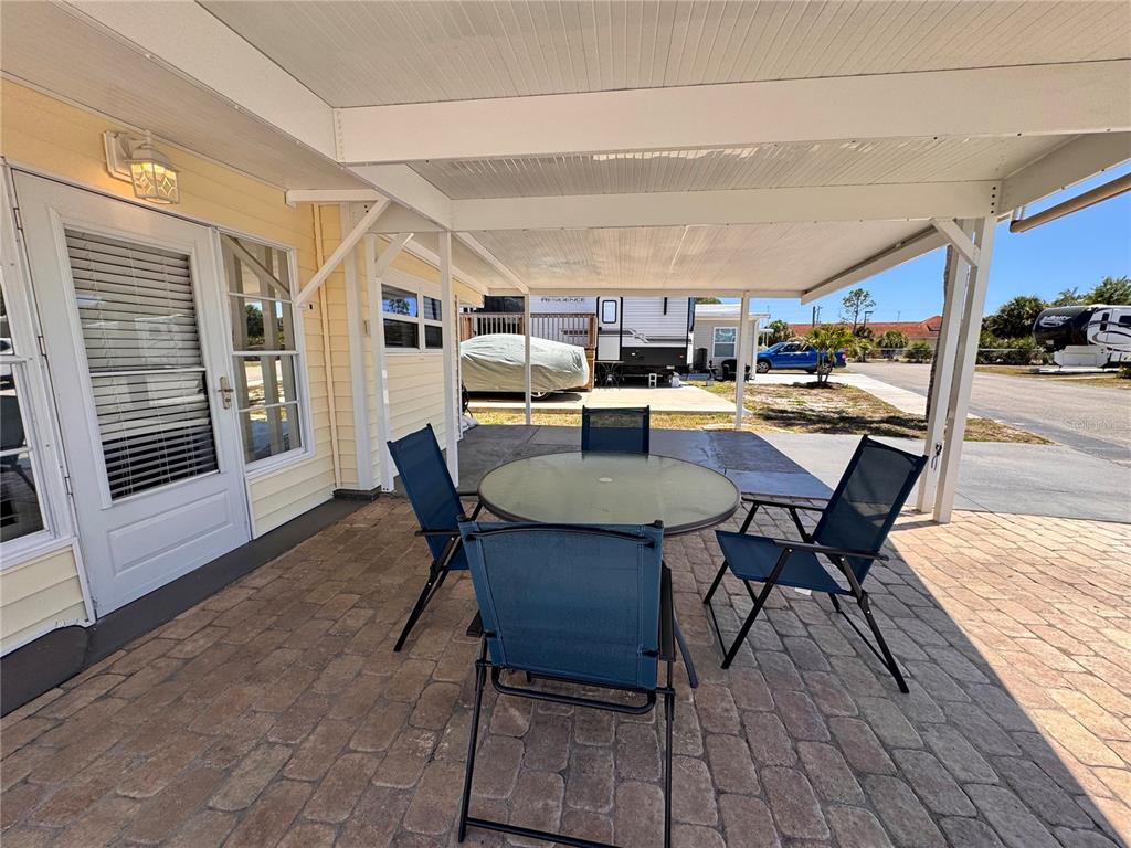 A covered patio features a glass-top table with four chairs on a paved surface — 1475 FLAMINGO DRIVE UNIT 128, ENGLEWOOD, FL