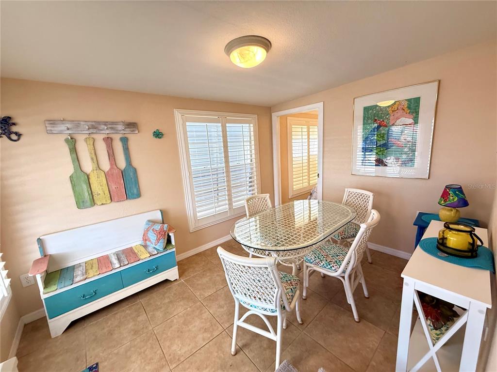 A dining room features a glass-topped table, white chairs, a bench, and coastal-themed wall decor — 1475 FLAMINGO DRIVE UNIT 128, ENGLEWOOD, FL