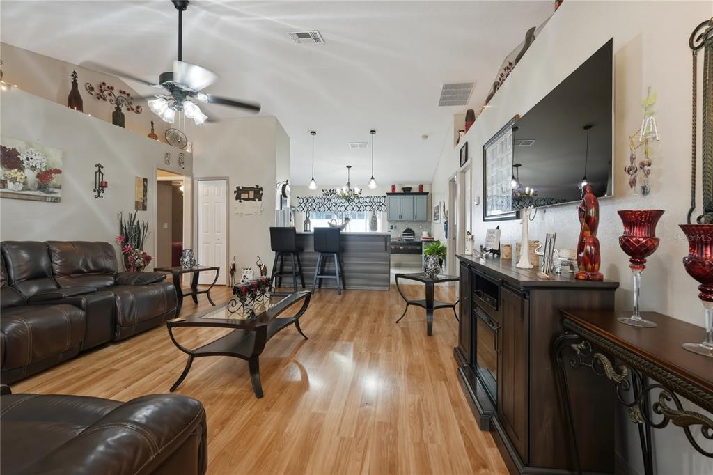 A living room with wood-look flooring, a leather sofa, and an open view to the kitchen — 1909 CONCH LANE, KISSIMMEE, FL
