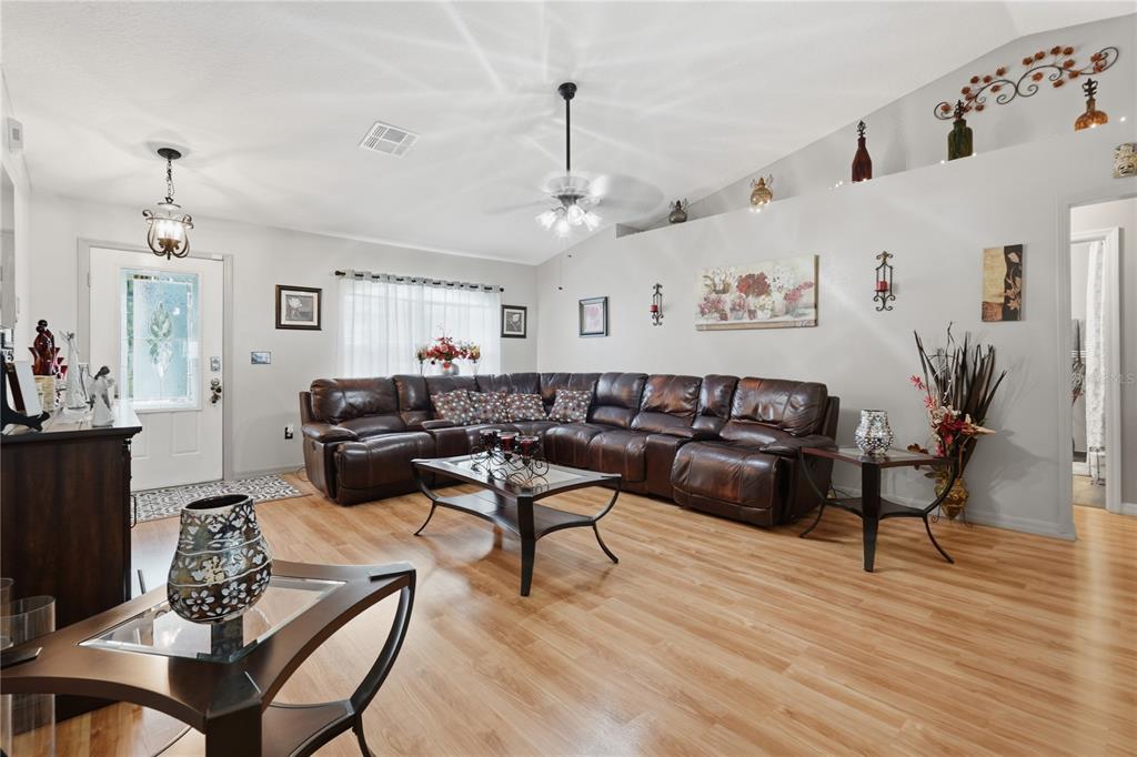A living room features a large brown leather sectional, wood-look flooring, and a vaulted ceiling — 1909 CONCH LANE, KISSIMMEE, FL
