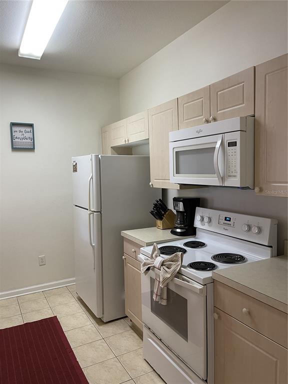 A kitchen features light wood cabinets, white appliances, and tiled flooring — 2306 SILVER PALM DRIVE UNIT 105, KISSIMMEE, FL