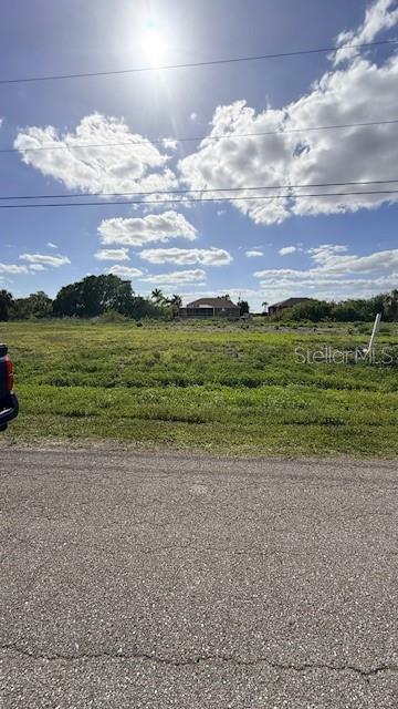 A view of a vacant, grassy lot from an adjacent paved road under a sunny sky — 1916 NE 23RD PLACE, CAPE CORAL, FL
