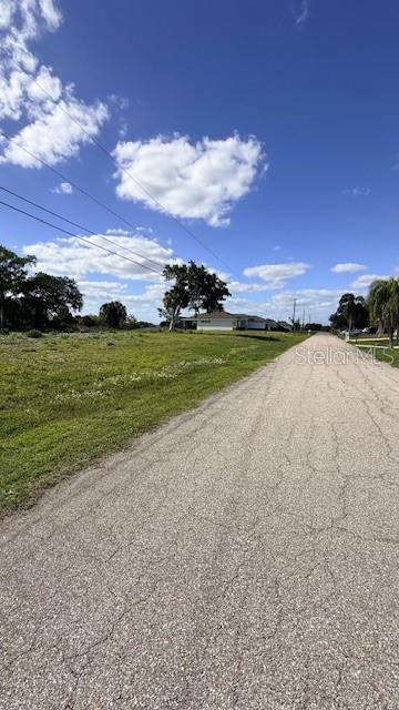 A paved road runs alongside a grassy vacant lot with trees and houses in the distance — 1916 NE 23RD PLACE, CAPE CORAL, FL
