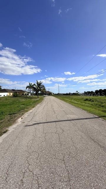 A paved road stretches toward houses and palm trees under a bright blue sky — 1916 NE 23RD PLACE, CAPE CORAL, FL