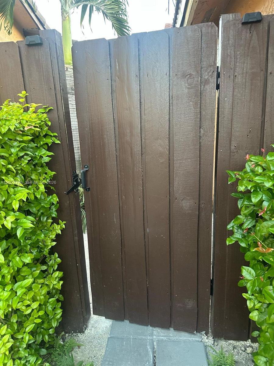 A dark brown wooden gate stands between two green bushes on a paved walkway — 1115 SW 136th Pl # 2, Miami FL 33184, MIAMI, FL