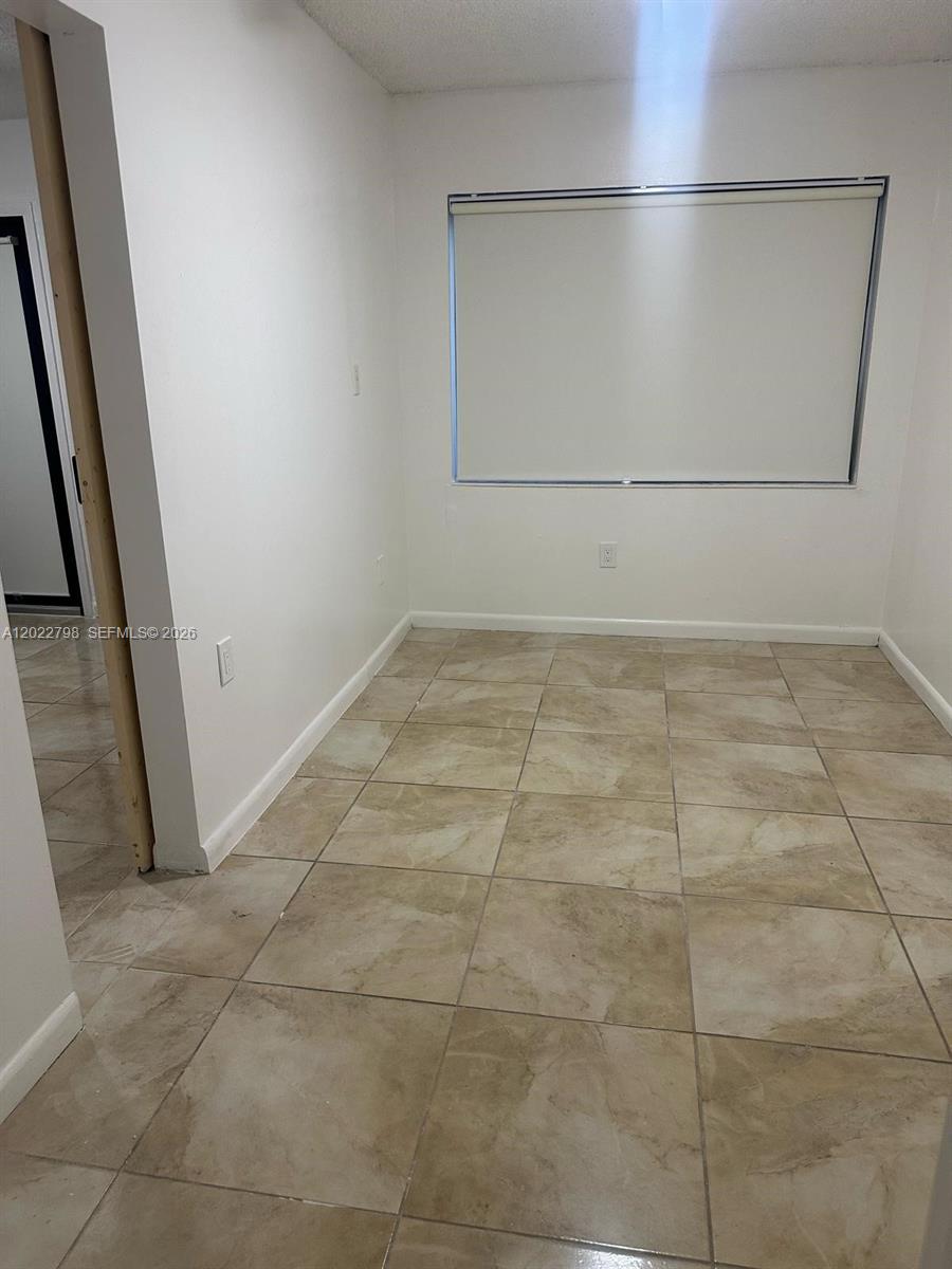 An empty room features light-colored walls, large square floor tiles, and a window with a shade — 1115 SW 136th Pl # 2, Miami FL 33184, MIAMI, FL
