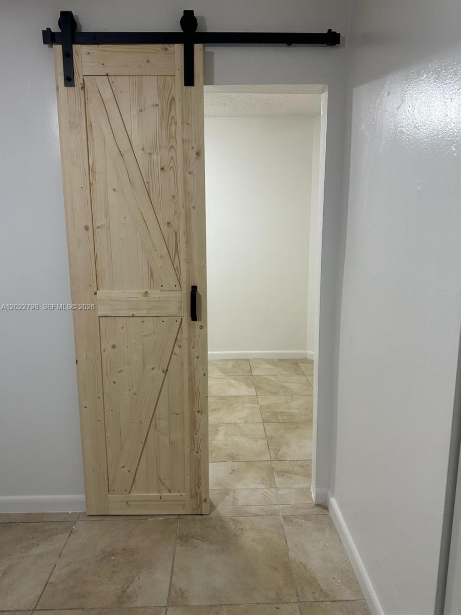 A light wood barn door with black hardware is installed on a white wall — 1115 SW 136th Pl # 2, Miami FL 33184, MIAMI, FL