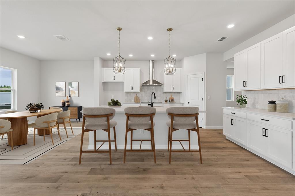 A modern kitchen features white cabinets, a dark blue island, stainless steel appliances, and wood flooring — 15235 EASTLYN DRIVE, BRADENTON, FL