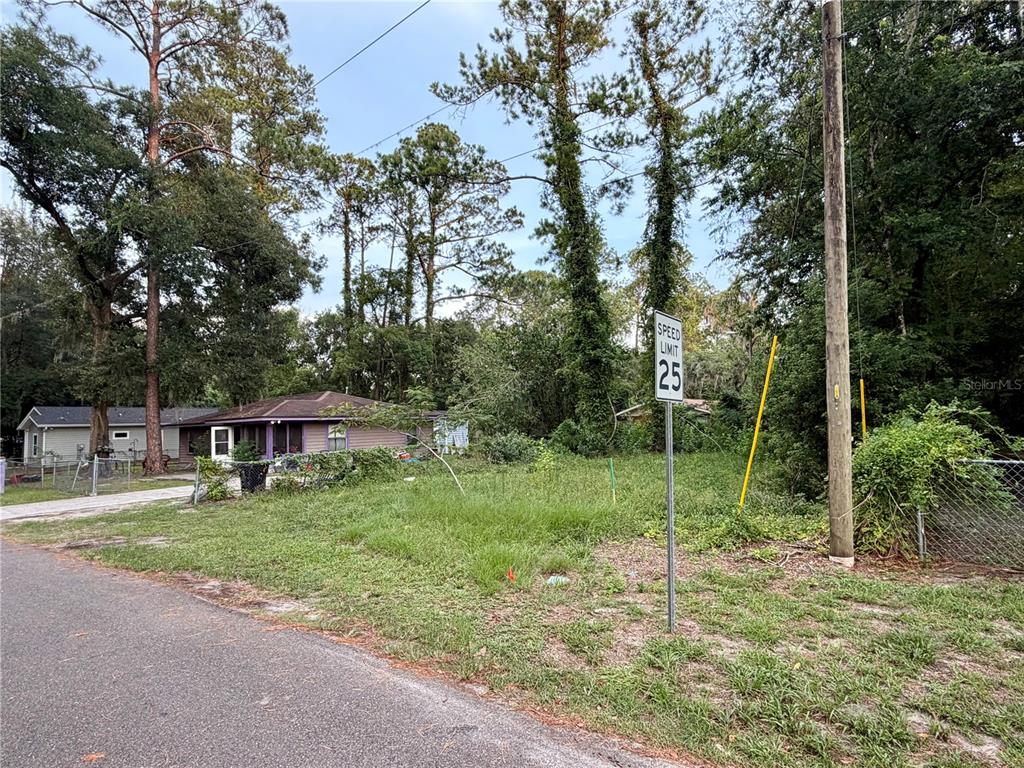 A vacant, grassy lot sits next to a small house with a purple exterior — XX NE 6TH AVENUE, GAINESVILLE, FL