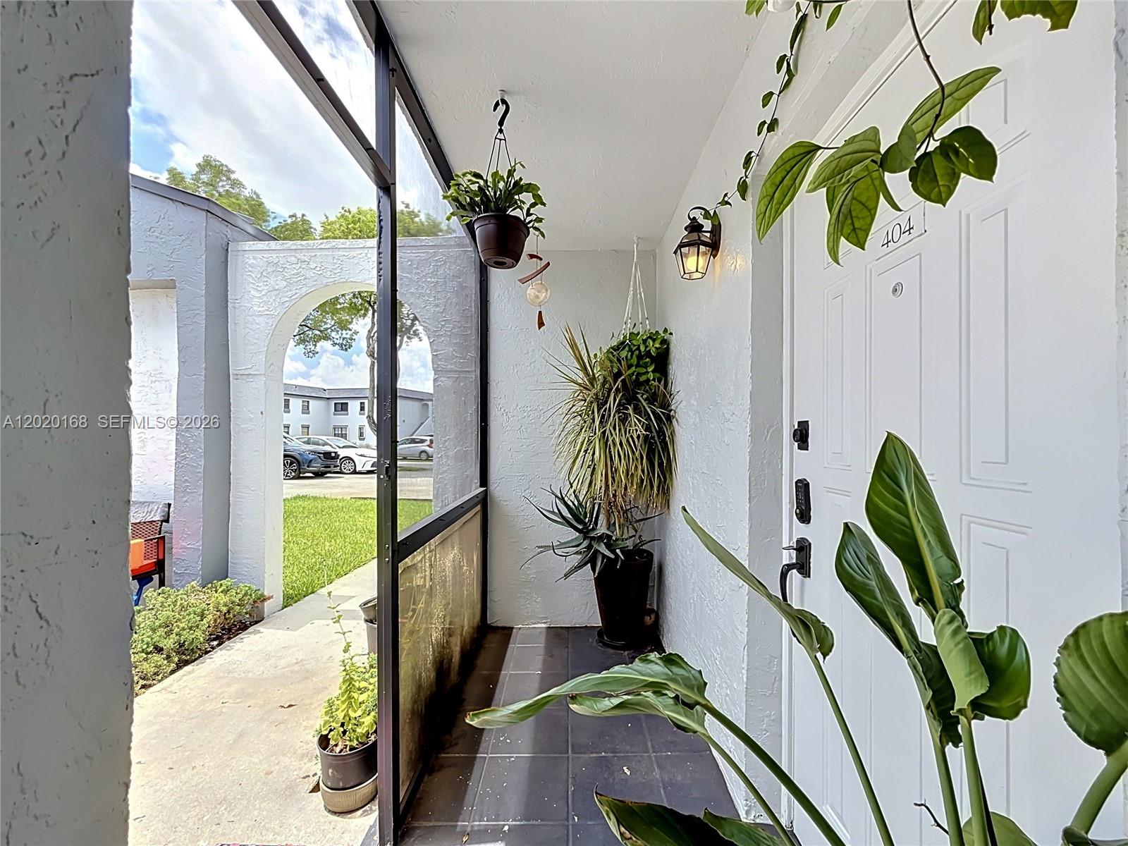 A screened-in porch features a white door, hanging plants, and a view of a parking lot — 18296 Mediterranean Blvd # 404, Hialeah FL 33015, HIALEAH, FL