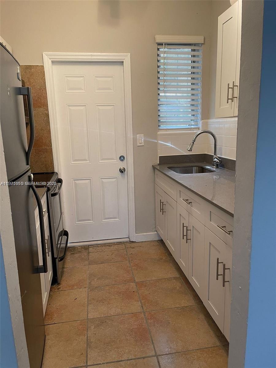 A narrow kitchen features white cabinets, a stainless steel sink, and a white exterior door — 1346 NW 6th St # 4, Miami FL 33125, MIAMI, FL