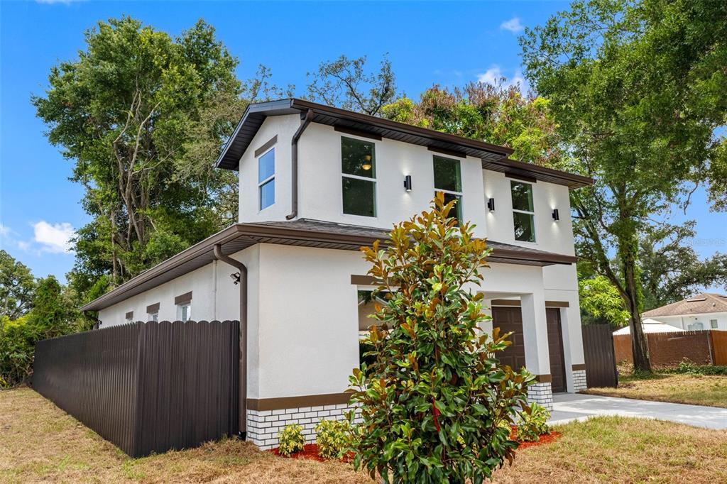 A two-story white house with brown trim and a dark fence stands on a lawn — 2405 E 23RD AVENUE, TAMPA, FL